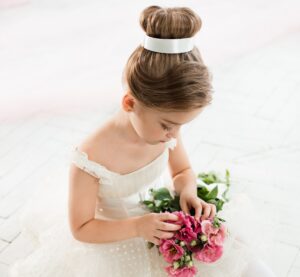 The little balerina in white tutu in class at the ballet school sitting on the wooden floor with flowers